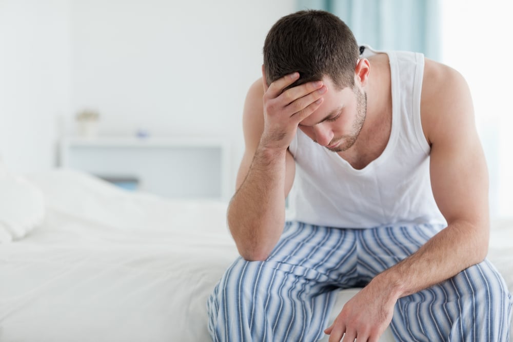 Ill man sitting on his bed with his head on his hand